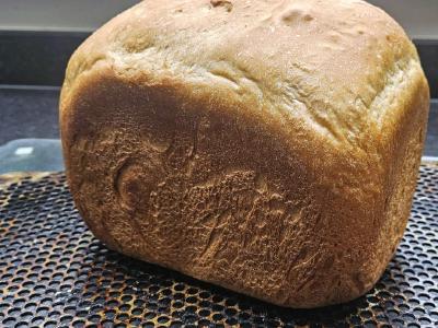 Whole baked white loaf from a bread machine, cooling on a perforated tray.